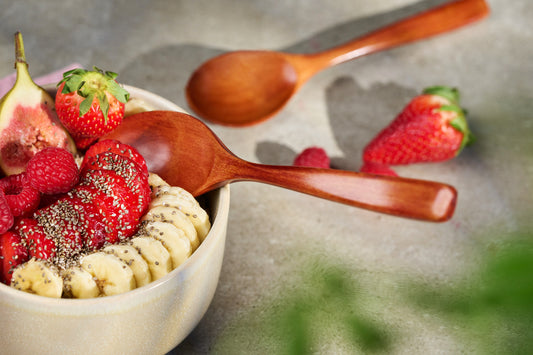 Zwei Bambuslöffel an einer Frühstücksbowl mit Erdbeeren, Himbeeren, Banane und Chiasamen