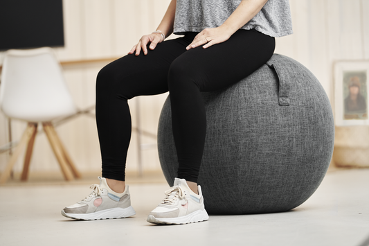 Person sitzt auf dem grauen Treasy Home Office Sitzball mit Stoffbezug – ergonomisches, aktives Sitzen für eine gesunde Haltung im Büro.