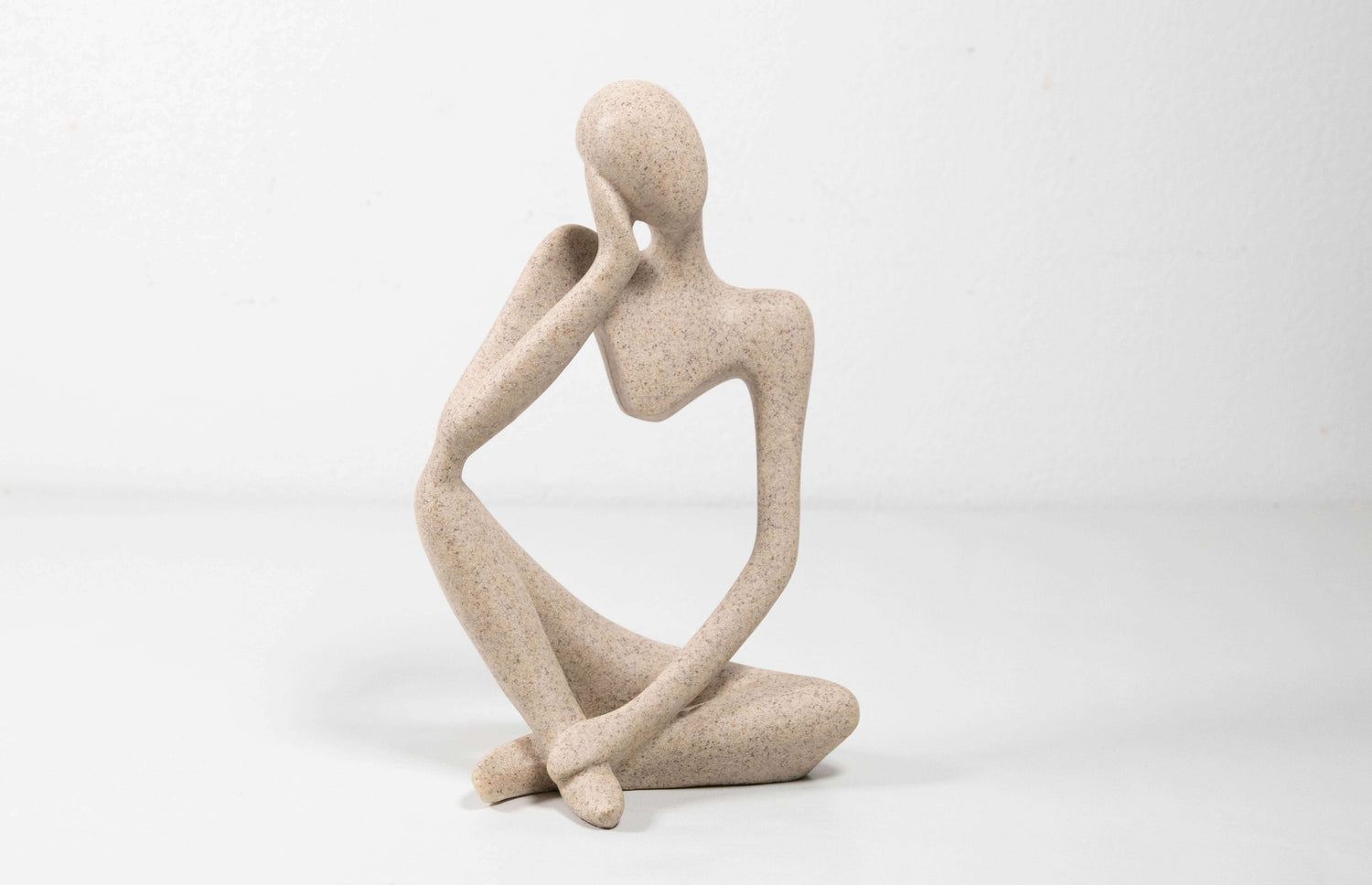 Abstrakte Figur aus Kunstharz in heller Steinoptik, die in sitzender Pose mit nachdenklicher Haltung dargestellt ist. Die sanft geschwungene Form und glatte Oberfläche verleihen der Skulptur eine elegante, moderne Ausstrahlung.