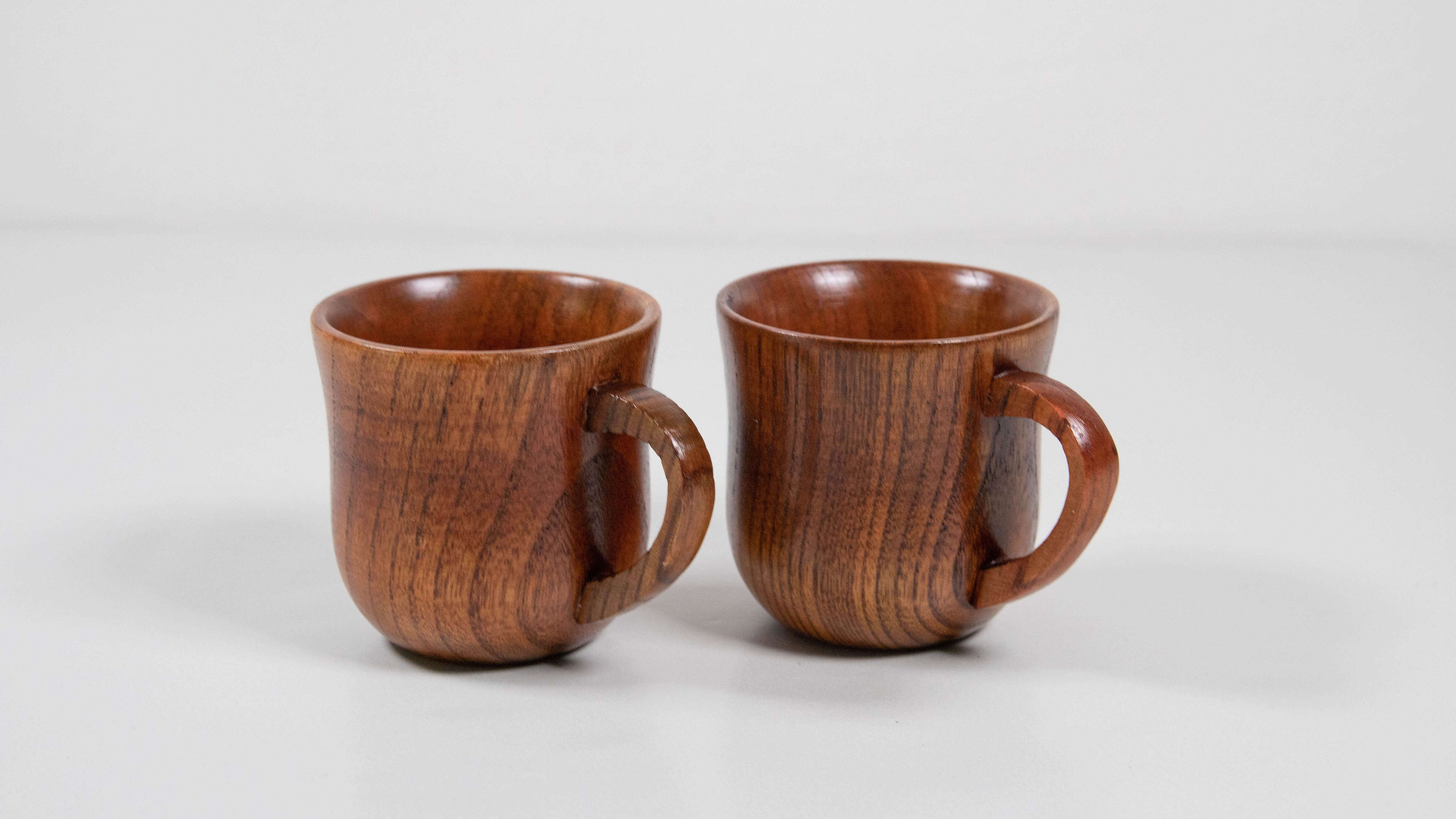 Das Bild zeigt zwei handgefertigte Becher aus Jujube-Holz auf hellem Untergrund. Ihre sanft geschwungene Form, der warme Farbton und die natürliche Maserung des Holzes verleihen ihnen eine edle, harmonische Ausstrahlung. Durch die glatte Oberfläche und den ergonomischen Griff liegen sie angenehm in der Hand – perfekt für Espresso, Tee oder als stilvolle Deko-Elemente.