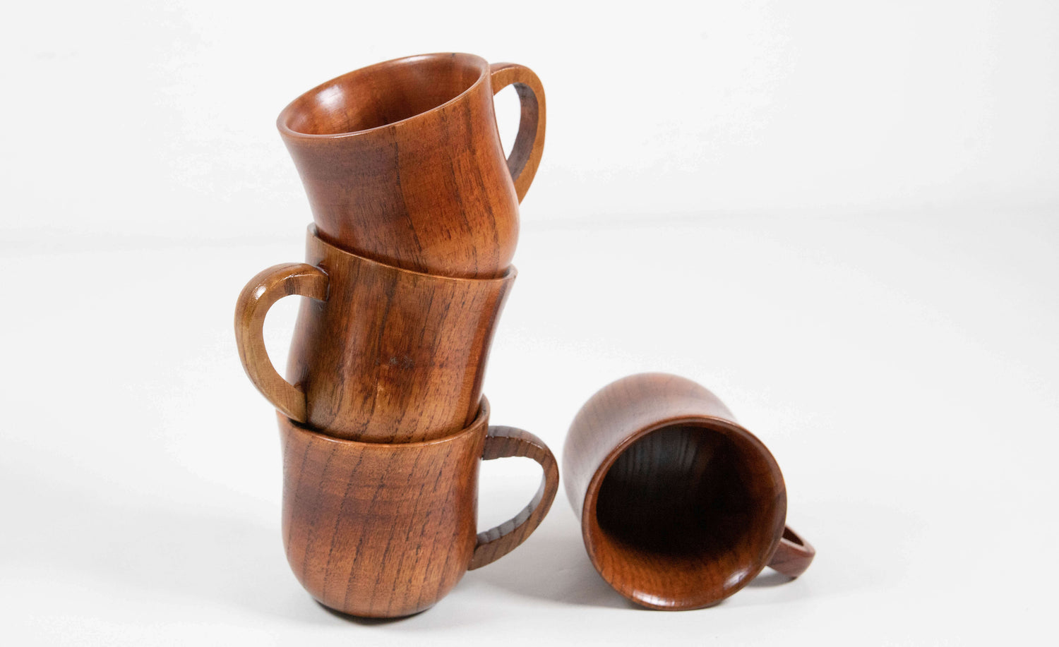 Das Bild zeigt vier Becher aus Jujube-Holz, von denen drei kunstvoll übereinander gestapelt sind, während einer seitlich liegt. Die Becher strahlen durch ihre feine Maserung und den warmen, rötlich-braunen Ton eine natürliche Eleganz aus. Das stapelbare Design wirkt modern und funktional – perfekt für ein harmonisches Tischarrangement mit handwerklichem Charakter.