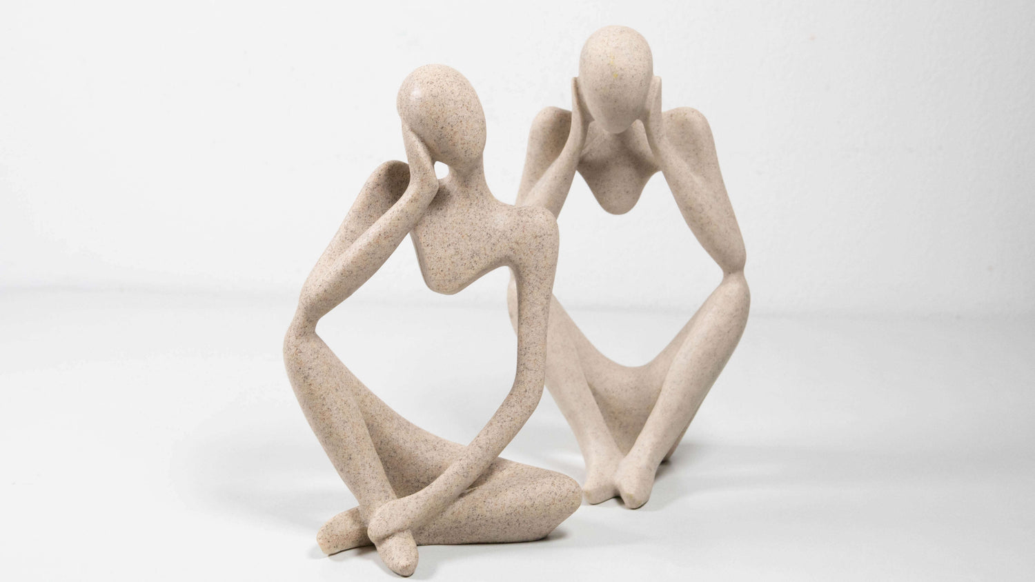 Zwei moderne Figuren aus Kunstharz sitzen in nachdenklicher Pose nebeneinander. Die abstrakt geformten Körper haben eine glatte, steinähnliche Oberfläche in hellem Beigeton und strahlen Ruhe und Minimalismus aus.